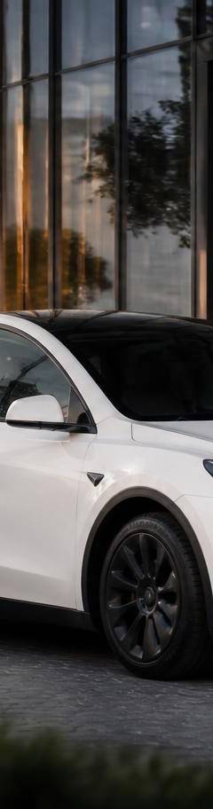 White Tesla Model Y chauffeur car with professional driver outside a DIFC office tower in Dubai at golden hour