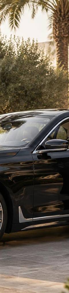 Professional chauffeur opening a black BMW 7 Series at an Emirates Hills villa in Dubai